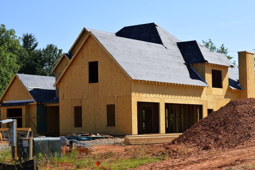 brown-and-gray-wooden-2-storey-house-near-tree-209266 A partially built wooden house under construction, showcasing its progress and design in daylight.